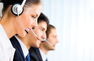 Three happy smiling young customer support phone operators at workplace